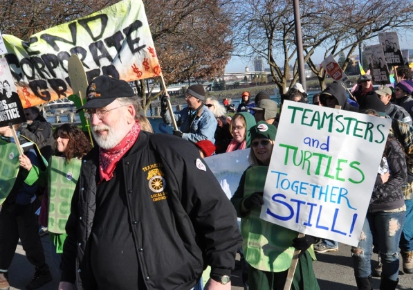 A group of protesters march in Seattle, holding signs that advocate for labor activists and environmentalists to work together.