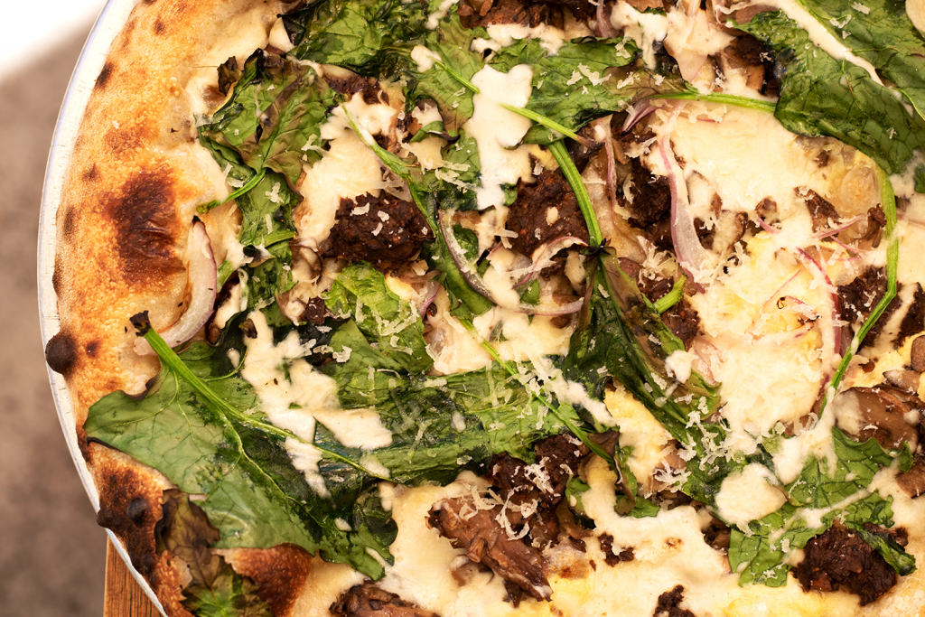 A vegan pizza features vegan cheese melted over arugula