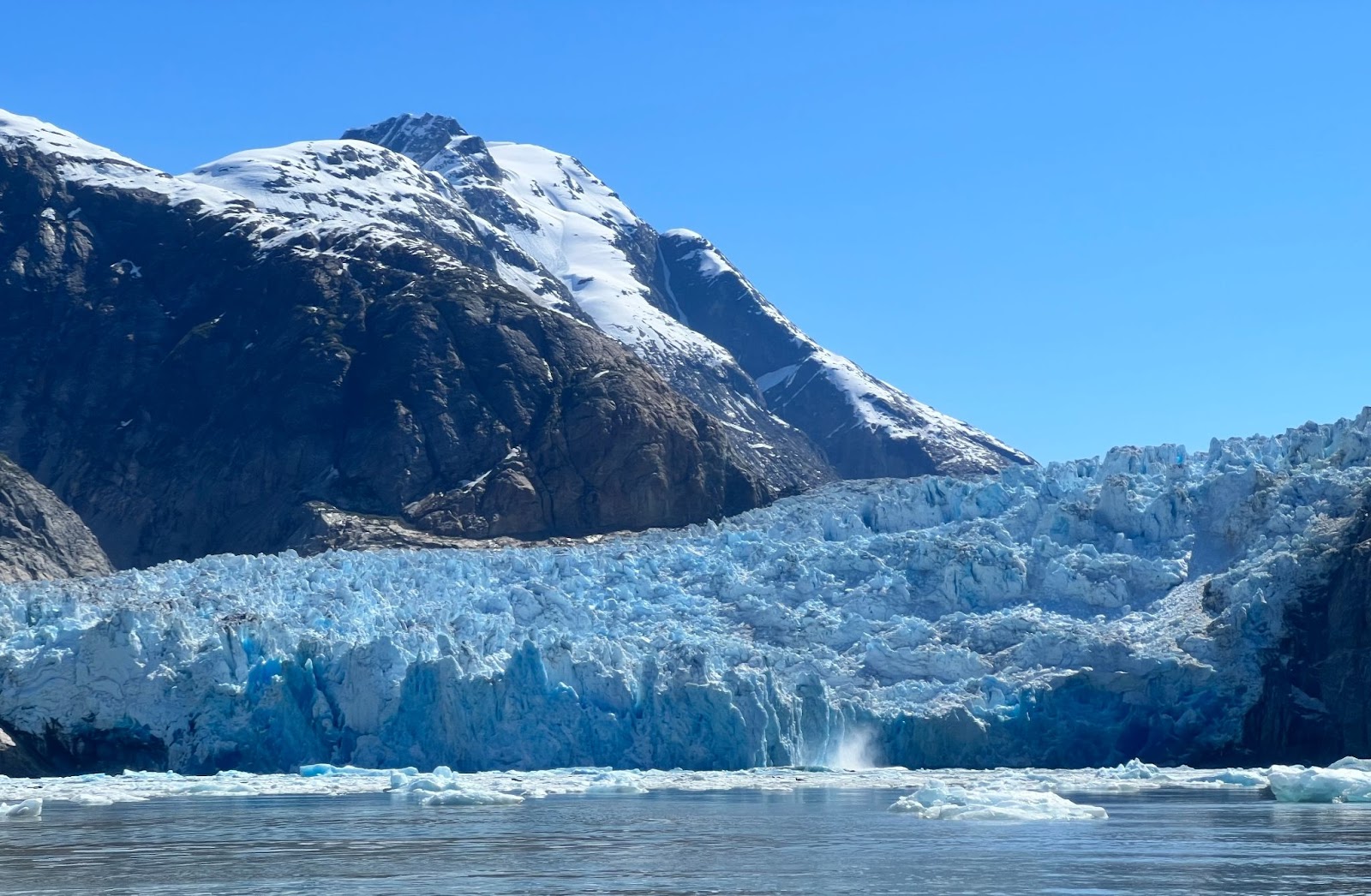 A close-up view of a glacier from the water, looking up at the steep, rocky valley left in its wake.